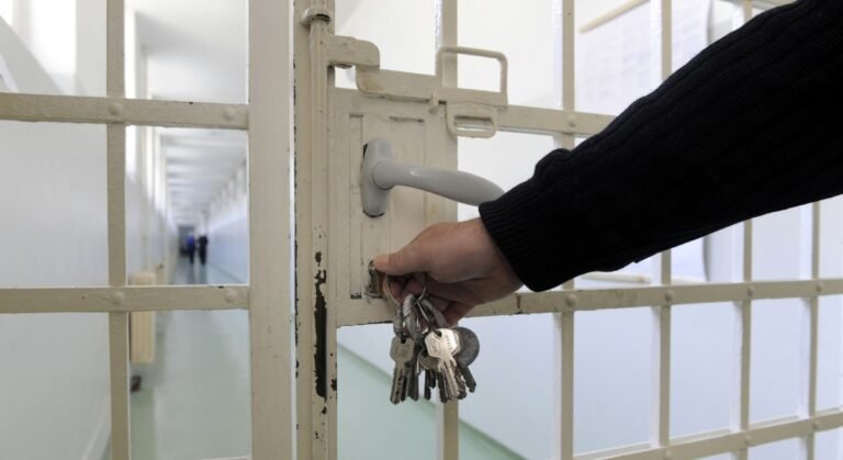 Gros plan d’une main tenant un trousseau de clés en train de refermer une grille à l’intérieur d’un établissement pénitentiaire