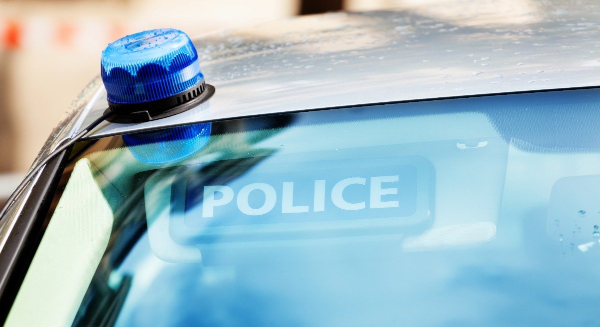 Gros plan sur le pare-brise d’un véhicule de police avec le mot « Police » visible sur le pare-soleil et un girophare posé sur le toit